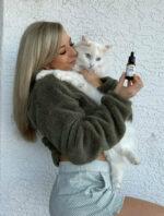 A young woman holding a cat in one hand and the product in the other.