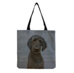 A denim colored canvas tote bag with a picture of a black labradoodle with woven black straps.