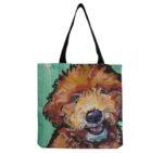 A seafoam green colored canvas tote bag with a painted image of a golden doodle with woven black straps.