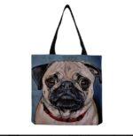 A denim colored canvas tote bag with a picture of Pug with woven black straps.